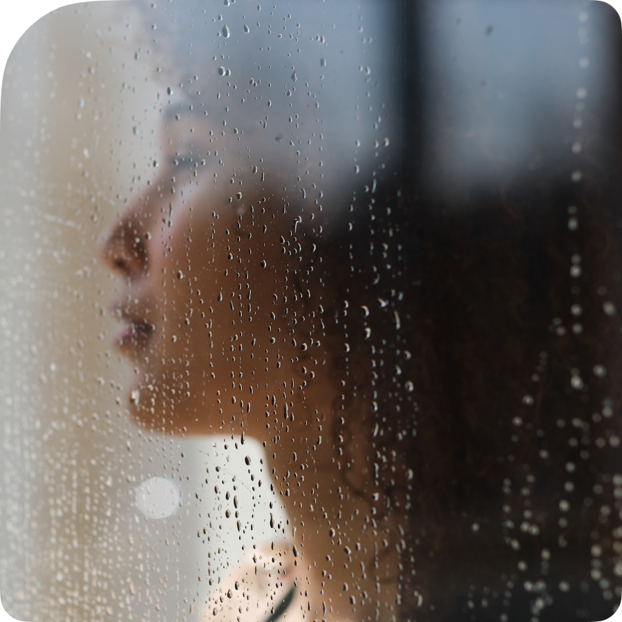 Woman behind glass with rain looking out a window-900x900